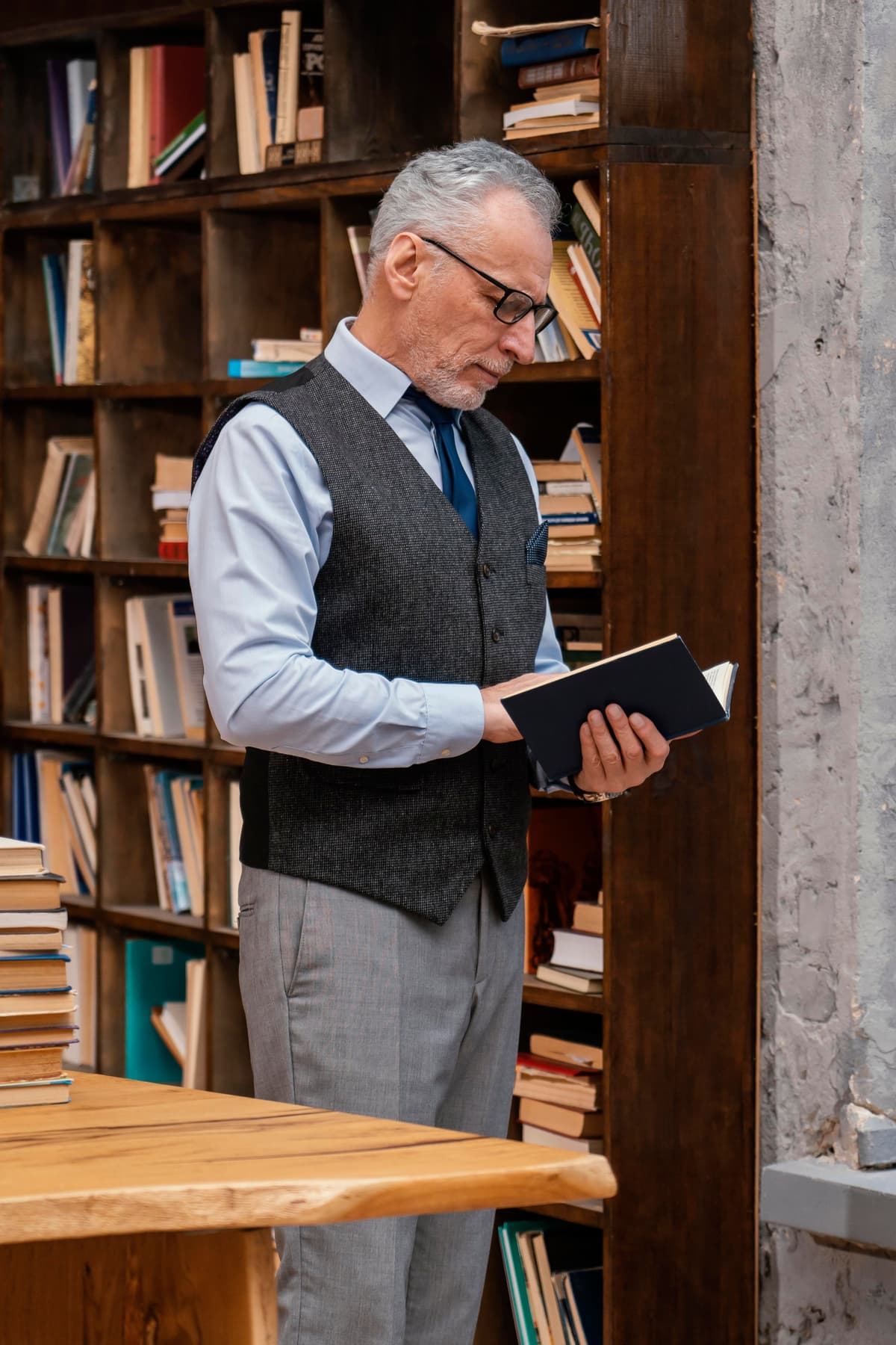 Older gentleman with glasses reading a book in library